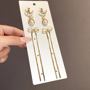 Dettaglio di eleganti orecchini a nappa con fiocco dorato, strass e perle raffinate