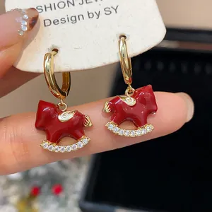 Close-up detail showing red enamel rocking horse earrings with gold plating and zircon
