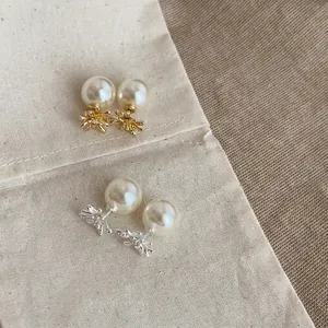 Dettaglio di orecchini a perno con perle e fiori in oro e argento e zirconi.