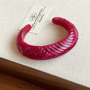 Bold wine red resin open cuff bangle with marbled texture and wavy geometric pattern.