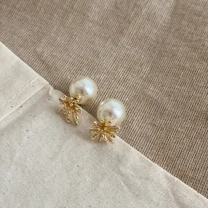Dettaglio di eleganti orecchini a lobo a fiore dorati con perle bianche su tessuto