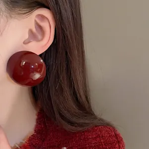 Oversized burgundy semi-circle stud earrings with high-gloss finish worn by an Asian model