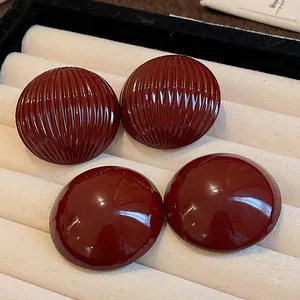 Close-up detail of deep red striped and smooth glossy half-round metal stud earrings.