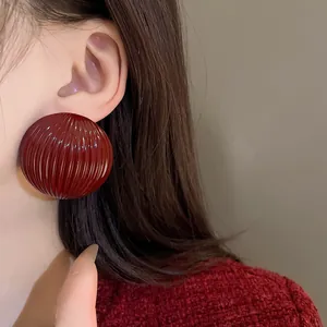 Close-up of exaggerated dark red semi-circle earrings with striped texture on model