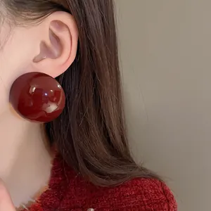 Close-up detail of a large burgundy glossy semi-sphere stud earring worn on ear
