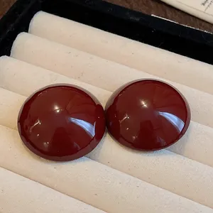 Close-up of glossy red domed stud earrings displayed in a cream jewelry tray