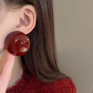 Close-up detail showing the glossy finish of a large burgundy round stud earring on ear