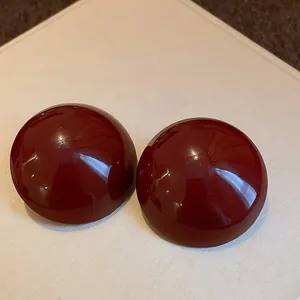 Detailed close-up of glossy dark red hemispherical stud earrings with a smooth polished finish