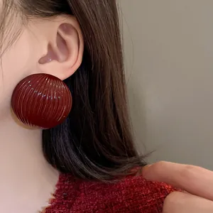 Close-up detail of a dark red ribbed semi-circular stud earring worn on model's ear.