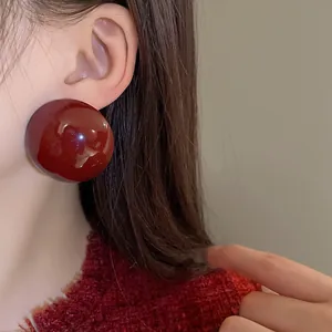 Macro detail shot of a glossy dark red oversized semi-sphere stud earring worn on model's ear