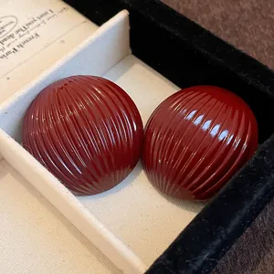 Detailed view of glossy deep red domed earrings with vertical striped texture in a box.