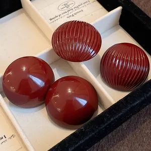 Close-up view of textured red striped and glossy oversized semi-circular stud earrings