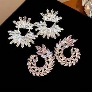 Sparkling leaf wreath and sunburst crystal stud earrings on black background.