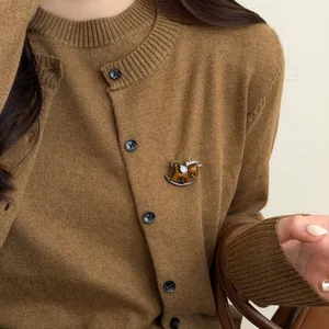 Detail of a brown flocked rocking horse brooch with rhinestones pinned on a knit cardigan