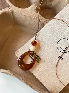 Close-up of an amber resin teardrop pendant on a brown cord against a rustic background.