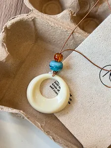 Close-up detail showing the circular resin pendant with marble and amber beads