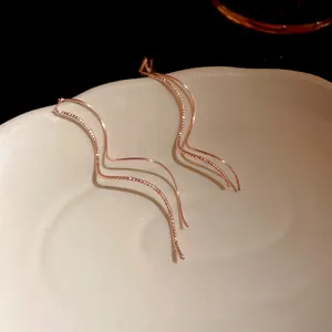 Detail of minimalist wave-shaped rose gold threader earrings showing smooth and textured finish