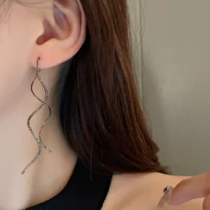 Close-up detail view of a long minimalist wavy geometric silver ear wire earring worn on ear