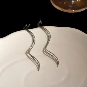 Close-up detail of elegant silver wave-shaped geometric earrings on a ceramic dish.