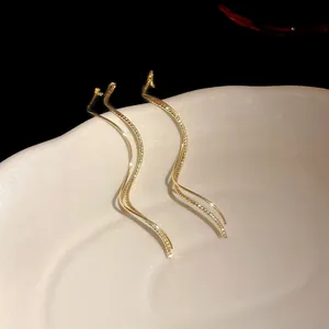 Close-up of gold-plated wave tassel earrings on a ceramic dish