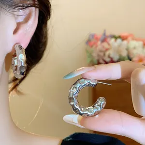 Detailed close-up view of a silver textured C-shaped hoop earring on a model's ear