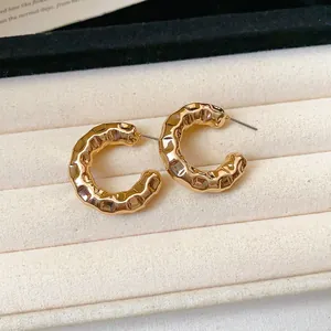 Detailed close-up of gold C-shaped chunky hoop earrings with a hammered textured finish.