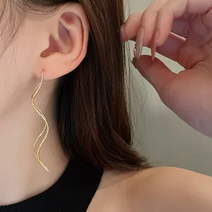 Close-up detail of elegant gold-plated wavy geometric drop earrings worn on model