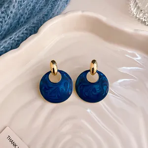 Dettaglio ravvicinato di orecchini vintage blu marmorizzati con perni dorati su vassoio.