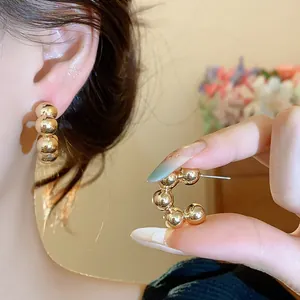Close-up of elegant gold beaded C-shaped stud earrings showing wearing effect.
