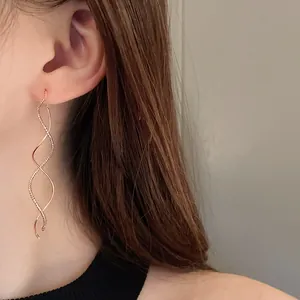 Detailed close-up of elegant gold plated wave spiral drop earrings on model's ear