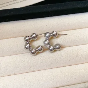 Detailed close-up shot of minimalist silver C-shaped beaded stud earrings in a soft tray.