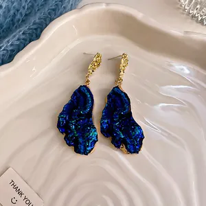 Dettaglio di orecchini di cristallo blu irregolari con accenti dorati testurizzati