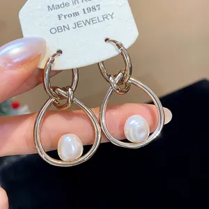 Primer plano de pendientes de nudo dorado con aros irregulares y perlas blancas