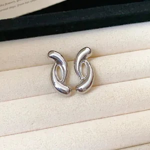 Detail of modern silver-tone curved earrings on a beige velvet jewelry tray.