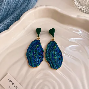Vista dettagliata di orecchini blu iridescenti con perni a forma di cuore verde.