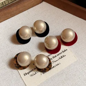 Detail of elegant round pearl stud earrings with velvet and leopard print backings.