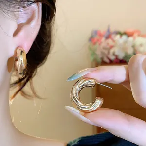 Detailed macro view of a gold C-shaped twisted hoop earring held by fingers and worn.