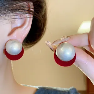 Detail view of round silver pearl stud earrings with red velvet backing worn on ear