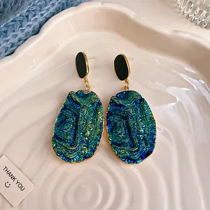 Dettaglio di orecchini pendenti ovali con una trama druzy iridescente verde acqua.