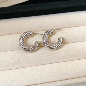 Detailed macro view of silver twisted croissant C-shaped hoop earrings on beige tray