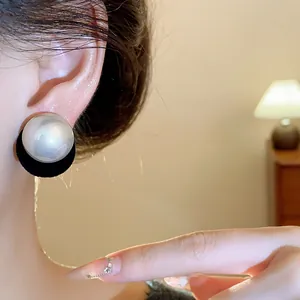 Close-up detail of large round pearl stud earring with elegant black backing on ear