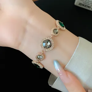 Vue rapprochée d'un bracelet de luxe en or rose avec des cristaux émeraude et gris au poignet.