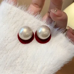 Macro detail of elegant round pearl stud earrings with red velvet base and silver needles.