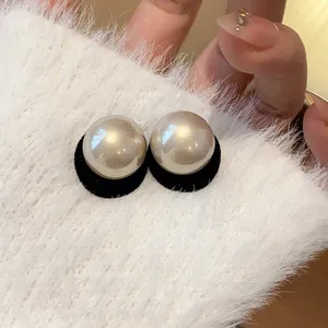 Close-up of champagne pearl stud earrings with black velvet base.