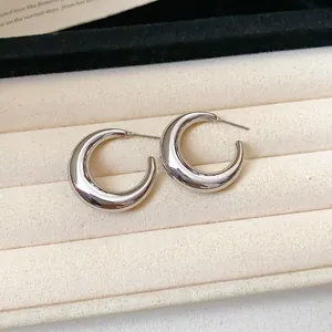 Close-up detail of minimalist silver-tone C-shaped hoop earrings on velvet tray