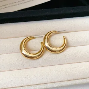 Detail view of chunky gold C-shaped hoop earrings resting in a beige jewelry box.