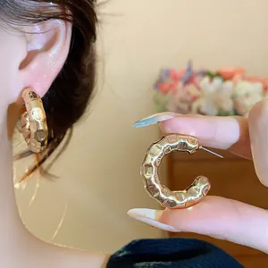 Close-up of golden C-shaped hoop earrings featuring a unique hammered texture finish.