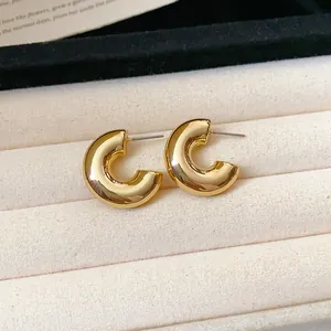 Close-up of minimalist gold C-shaped hoop stud earrings with glossy finish