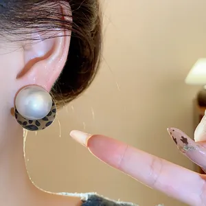Close-up view of a minimalist pearl earring with leopard print base worn on the ear