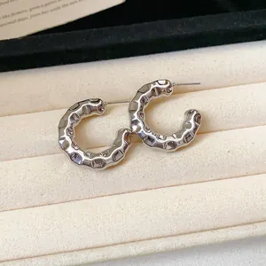 Close-up detail of silver C-shaped hoop earrings with hammered texture on cream fabric